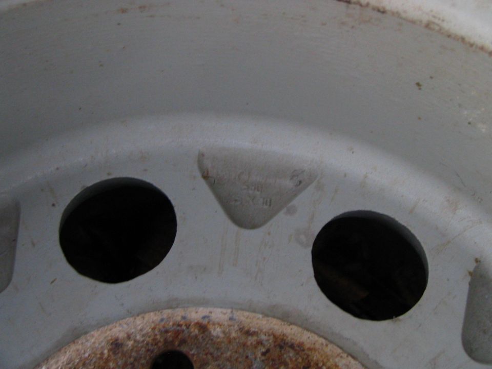 Gray wheel rim with two circular cutouts and embossed text. Rust is visible on the hub area