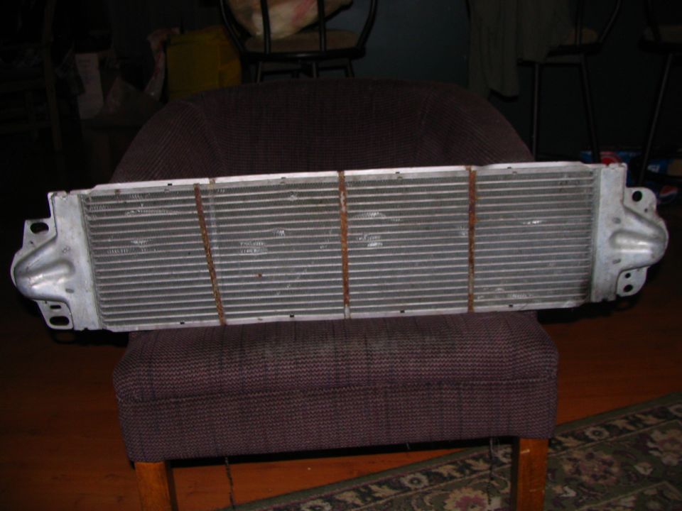 Aluminum radiator or intercooler with horizontal fins, held by brown straps, resting on a chair