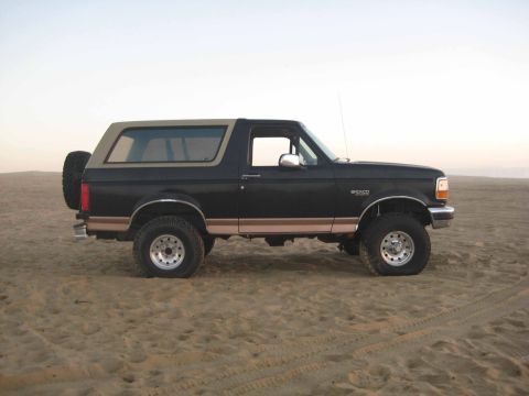 1994 Ford Bronco - A 1994 Ford Bronco sits on a sandy surface under a clear sky.