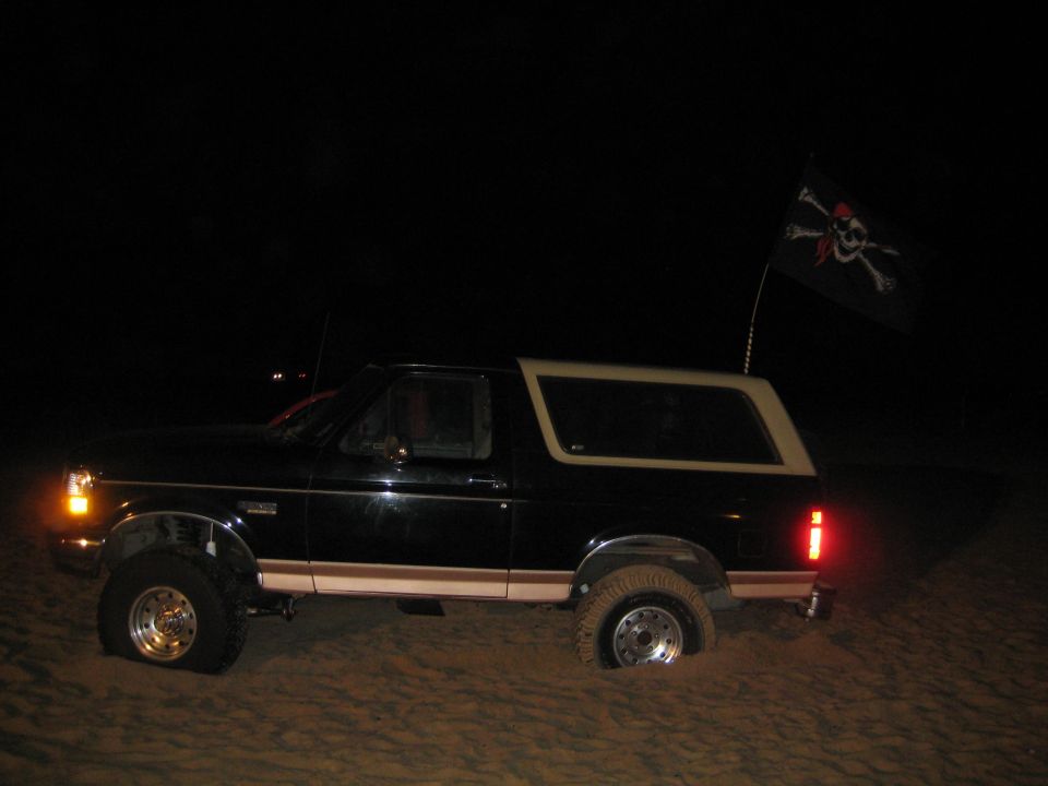 Black Ford Bronco with tan top stuck in sand, pirate flag on antenna
