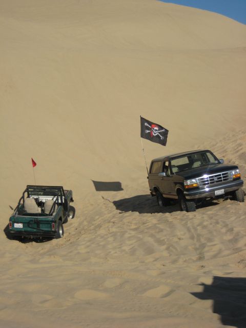 1994 Ford Bronco - Two SUVs, including a 1994 Ford Bronco, navigate sandy terrain with flags flying.