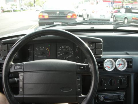 1990 Ford Mustang - View from inside a car, looking at the dashboard and the road ahead with other vehicles.