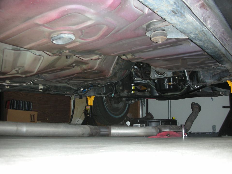 Undercarriage view of a vehicle, showing the exhaust system and frame components. The vehicle is supported by jack stands