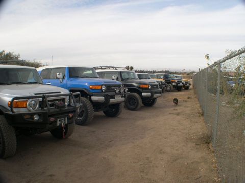 2007 Toyota FJ Cruiser - A line of Toyota FJ Cruisers are parked on a dirt lot under a cloudy sky.