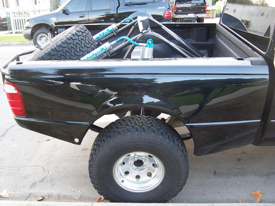 Black Ford Ranger pickup truck bed with spare tire, shocks, and fuel cell. Visible Supermotors.net logo