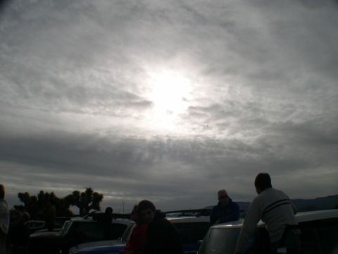 2007 Toyota FJ Cruiser - A group of people are gathered around several vehicles parked outdoors, with the sun partially obscured by heavy clouds.
