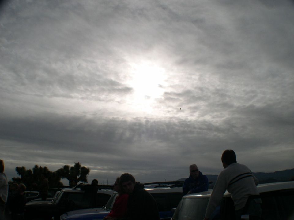 Several vehicles parked outdoors with people standing around them under a dramatic cloudy sky