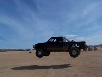 2007 Ford Ranger - A black pickup truck is captured mid-air during a jump over a dusty terrain.
