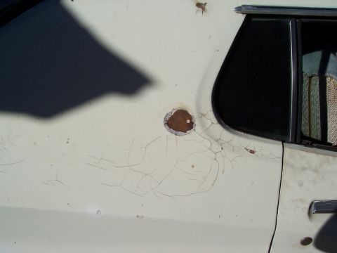 1972 Ford Ranchero - The paint on this vehicle's body panel is cracked, revealing rust around a circular imperfection.