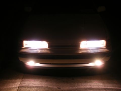 1991 Mazda MX-6 - The front of a car is illuminated by its headlights and fog lights in the dark.