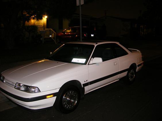 White LX-badged coupe parked at night under streetlights, front three-quarter view