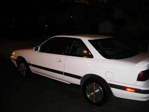 1991 Mazda MX-6 - A white 1991 Mazda MX-6 coupe is seen from the 3/4 front angle at night.
