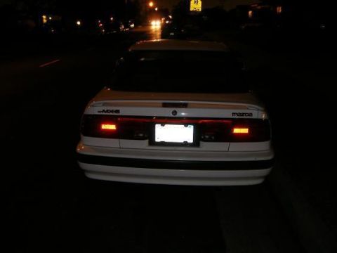 1991 Mazda MX-6 - Rear view of a white 1991 Mazda MX-6 at night, with illuminated taillights and a license plate area.