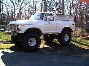 1986 Ford Bronco - This lifted Ford Bronco is parked on a dirt patch with trees in the background.