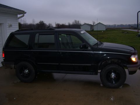 1996 Ford Explorer - Side view of a black SUV parked on a driveway in front of a house and a grassy field.