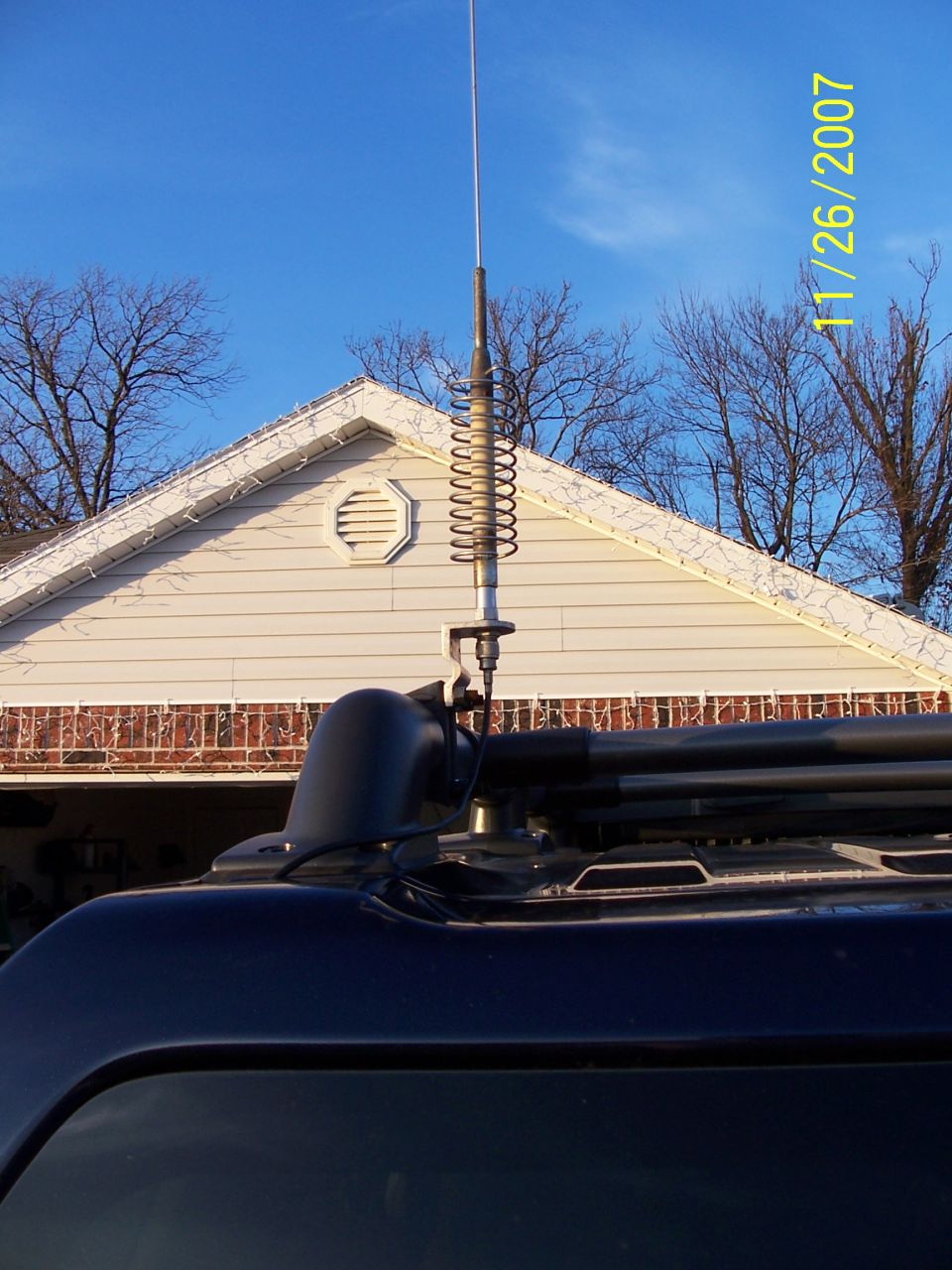 Coil-loaded whip antenna mounted on roof rack of dark blue SUV
