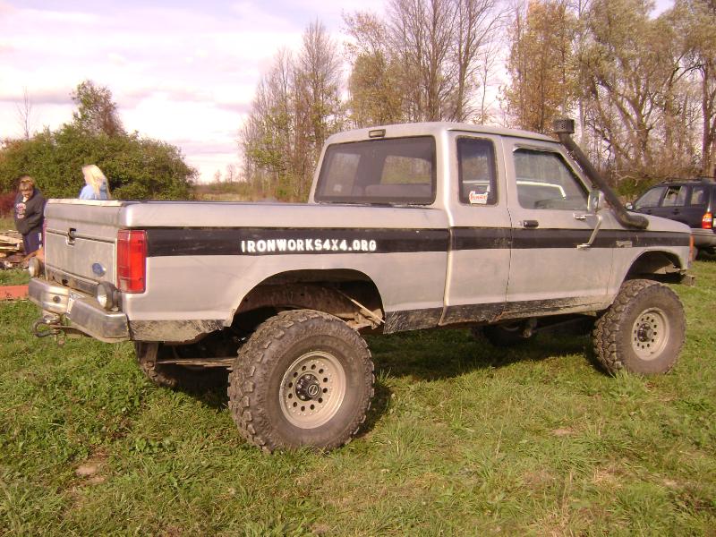 Silver lifted Ford 4x4 pickup with snorkel and tube rear bumper in a field
