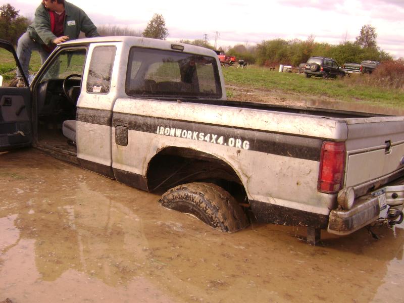 Silver Ford pickup stuck axle-deep in mud with IRONWORKS4X4.ORG decal on bedside
