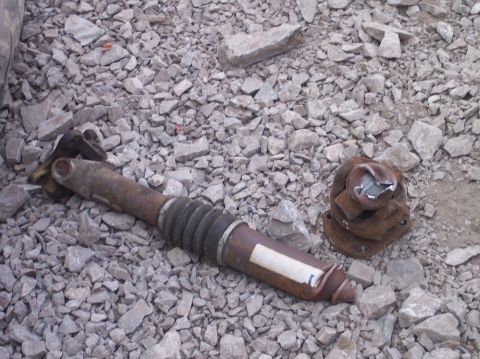 1995 Ford Bronco - A damaged driveshaft and differential flange lie on a bed of gravel, suggesting a significant mechanical failure.