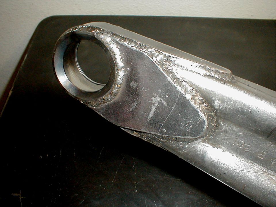 Close-up of a metal suspension component with visible welds and some stamped numbers