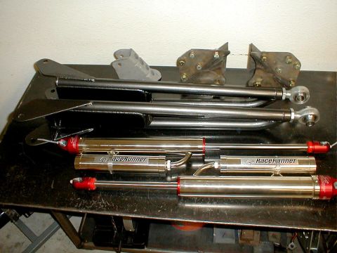 1996 Ford Bronco - Suspension components including control arms and RaceRunner shock absorbers are laid out on a metal workbench.