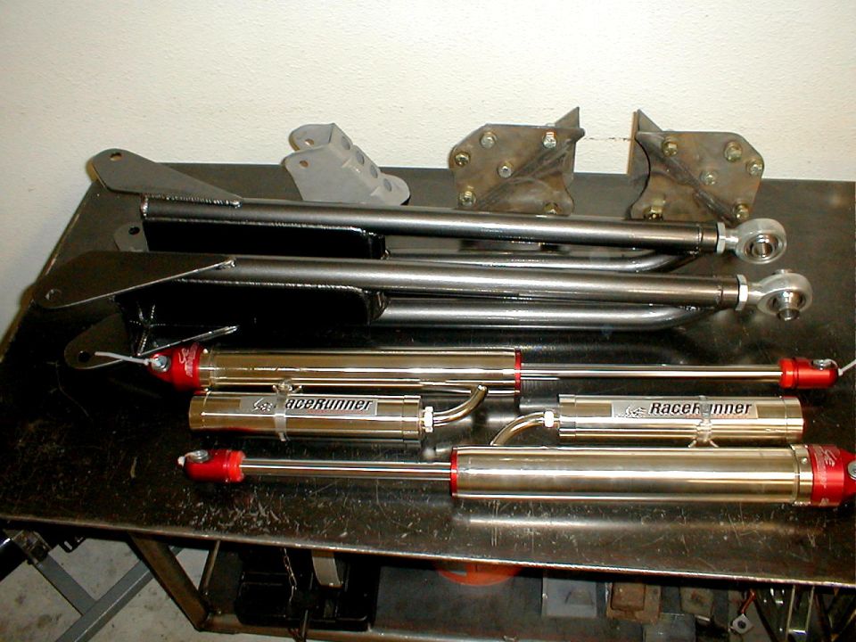 Two sets of suspension control arms and four shock absorbers with 'RaceRunner' branding on a workbench