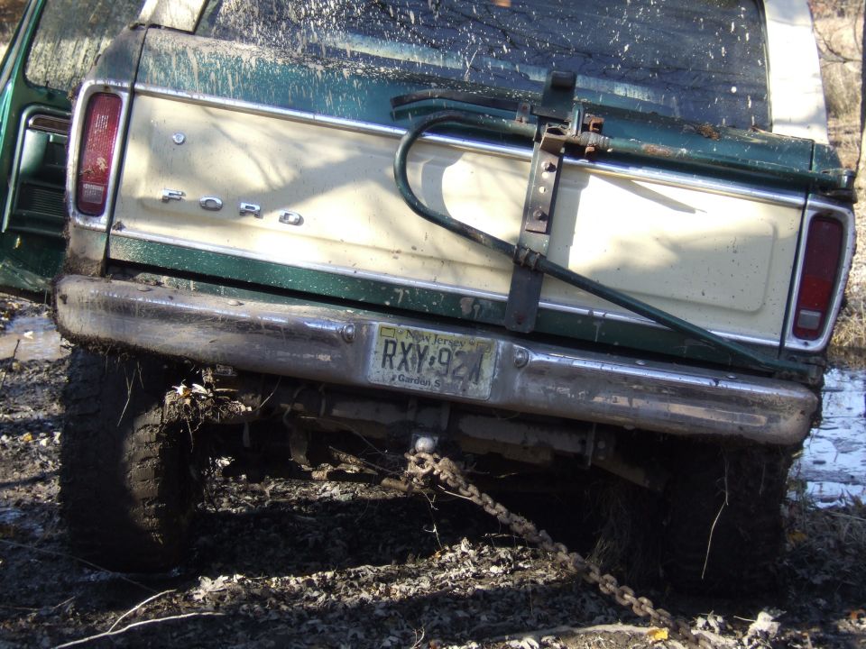 Rear view of a green and cream Ford pickup truck stuck in mud, with a New Jersey license plate