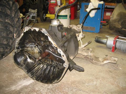1990 Ford Bronco - A transmission and tire are visible in a workshop setting, with various tools and equipment in the background.