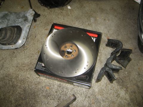 1990 Ford Bronco - A clutch disc and flywheel are laid out on a box, alongside other automotive parts.