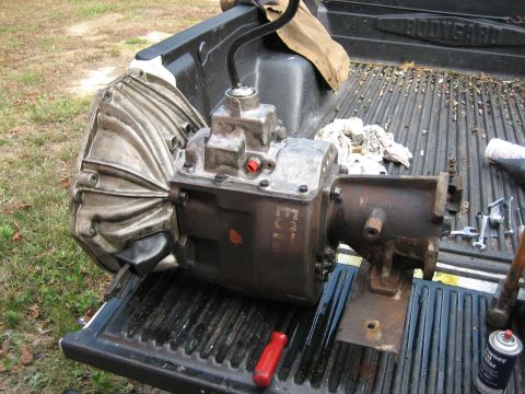 1990 Ford Bronco - Manual transmission assembly with shifter lever, resting in a pickup truck bed with tools nearby.