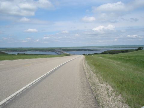 1989 Ford F-250 - A scenic view of a road leading to a bridge over a lake, with rolling green hills and a partly cloudy sky.