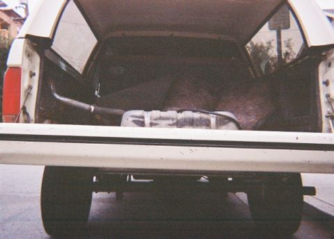 1991 Ford Bronco - Straight-on rear view into the open cargo area of a white SUV with the tailgate down and rear glass raised, showing the bare carpeted floor…
