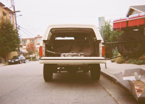 1991 Ford Bronco - Straight-on rear view of a white full-size Ford Bronco parked on a residential street with the tailgate down and rear glass up, exposing th…