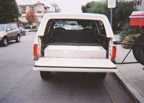 1991 Ford Bronco - Rear view of a 1991 Ford Bronco parked on a street, showing the open tailgate and a toolbox.