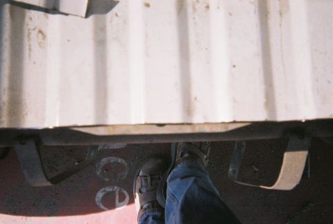 1991 Ford Bronco - A view from above looking down at the underside of a vehicle, showing feet standing on a red surface.