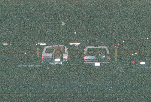 Two 1991 Ford Broncos parked side-by-side at night, one with a spare tire mounted on the rear door