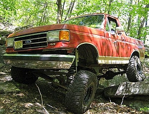 1986 Ford Bronco - This red pickup truck appears to be from the early 1980s, seen here navigating a rocky, wooded area.