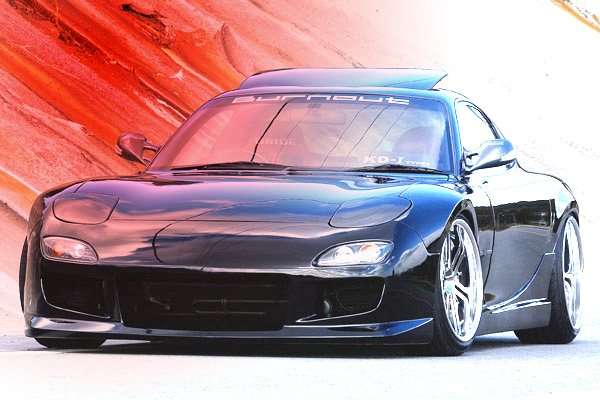 Front view of a modified black Mazda RX-7 with custom wheels and a "Burnout" sticker on the windshield