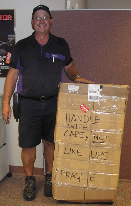1965 Ford Mustang - A man stands with a tall stack of boxes that have humorous handwritten instructions.