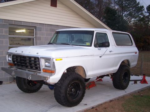 1979 Ford Bronco - White 1979 Ford Bronco lifted on jack stands in front of a garage.