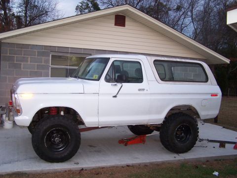 1979 Ford Bronco - This white SUV is elevated by a jack, showing its lifted suspension and large tires.