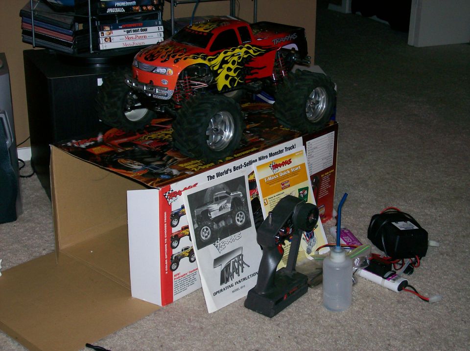 Red flamed Traxxas RC monster truck on its box with controller and fuel
