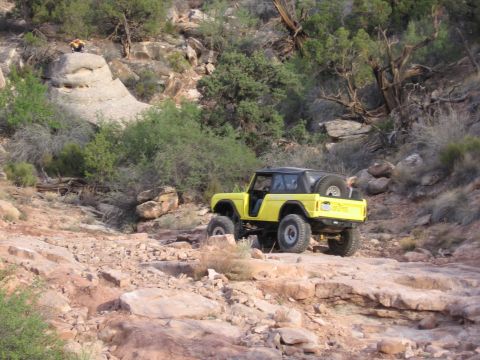 1979 Ford Bronco - A yellow SUV navigates a challenging rocky terrain with sparse vegetation.