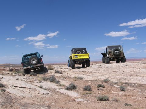1979 Ford Bronco - Three off-road vehicles, including a green 1978 Ford Bronco, navigate a rocky, desert landscape under a blue sky.