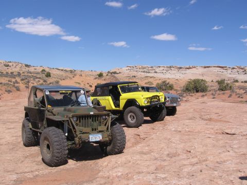 1979 Ford Bronco - Modified off-road vehicles are parked in a desert landscape with rocky terrain and distant hills.
