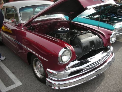 1998 Ford Crown Victoria - maroon early-1950s custom car sits with its hood open revealing a chromed V8 engine at an outdoor car show.