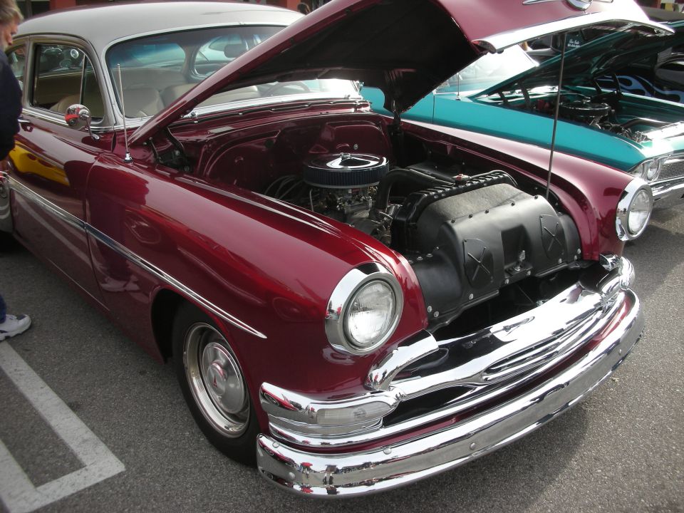 Maroon 1950s custom car with open hood and chromed V8 at a car show