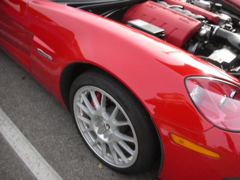 1998 Ford Crown Victoria - red front fender and silver multi-spoke wheel of a Corvette, with its red-topped engine visible under the open hood.