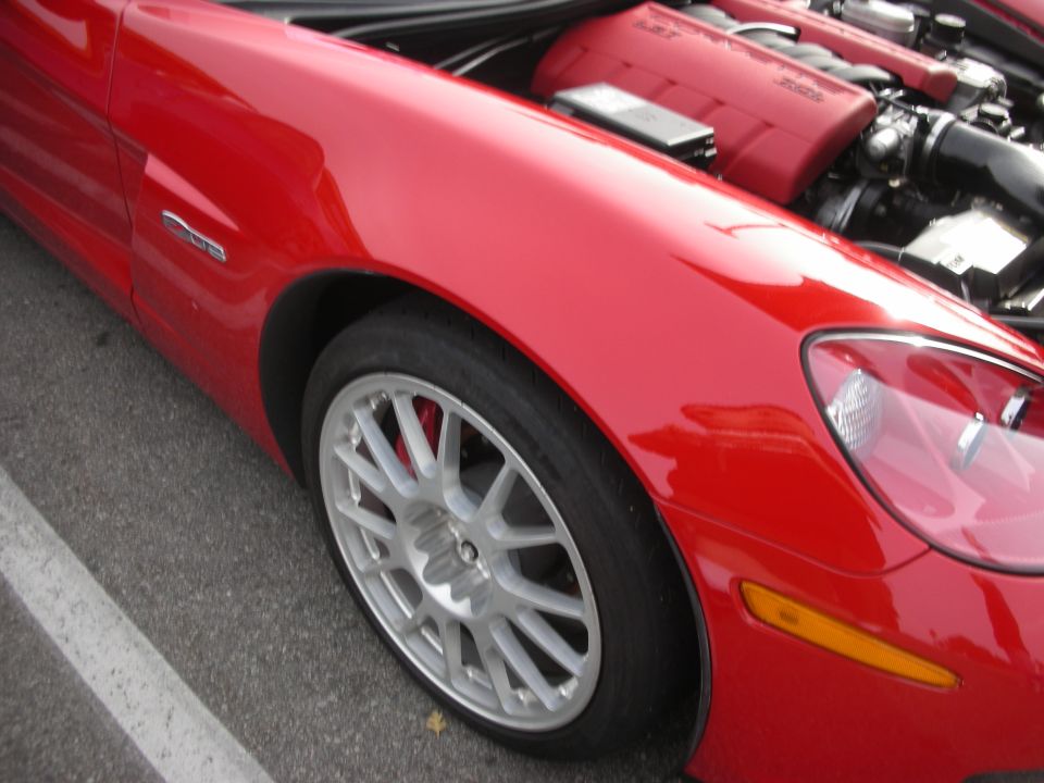 Front fender and silver wheel of a red Corvette with engine visible