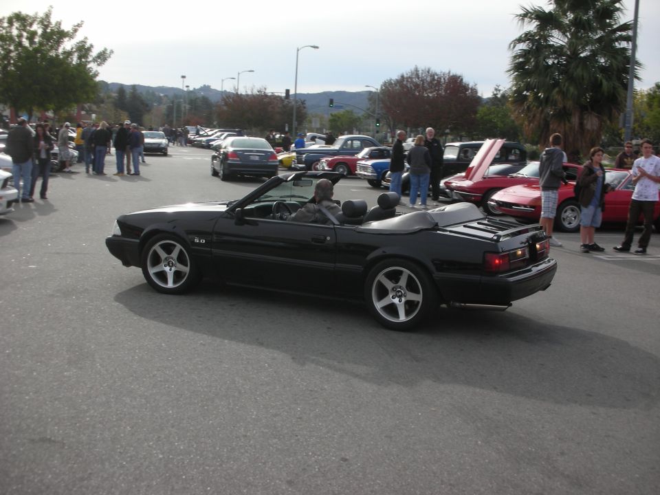 Black Fox-body Ford Mustang 5.0 convertible driving at a car show